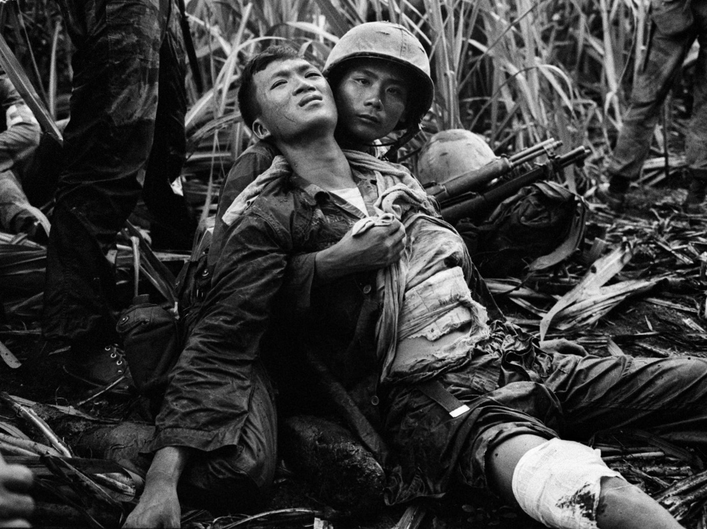 Foto van een vietnamese soldaat die een andere gewonde Vietnamese soldaat vasthoud.